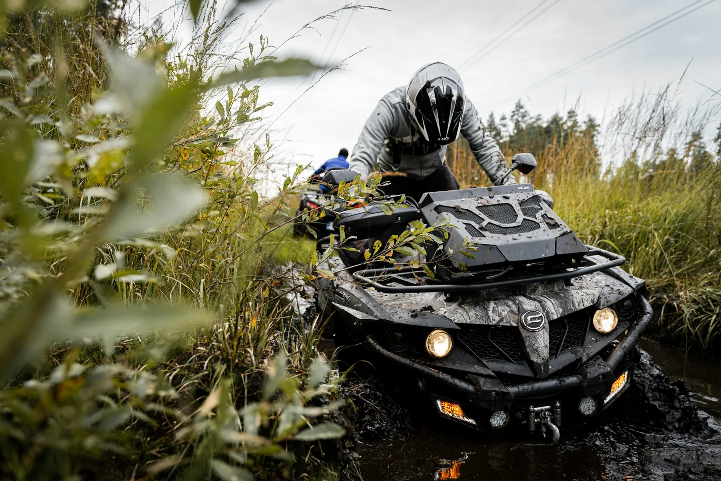 Utility ATV with a front rack pushing through a muddy forest trail